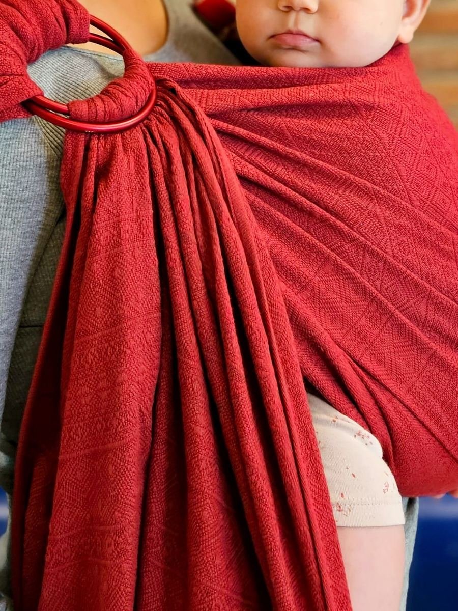 Baby sitzt geborgen im roten Ringsling auf der Hüfte